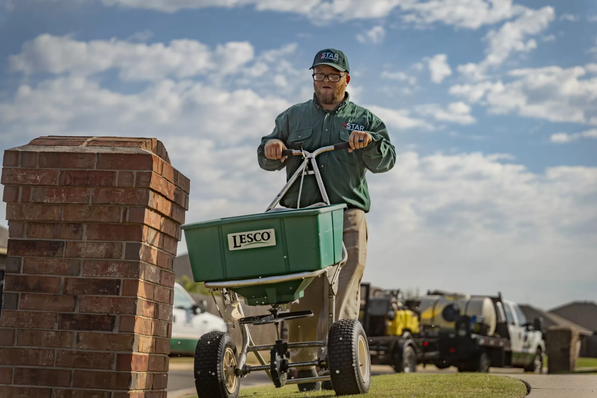 Lawn care technician spreading fertilizer with professional broadcast spreader